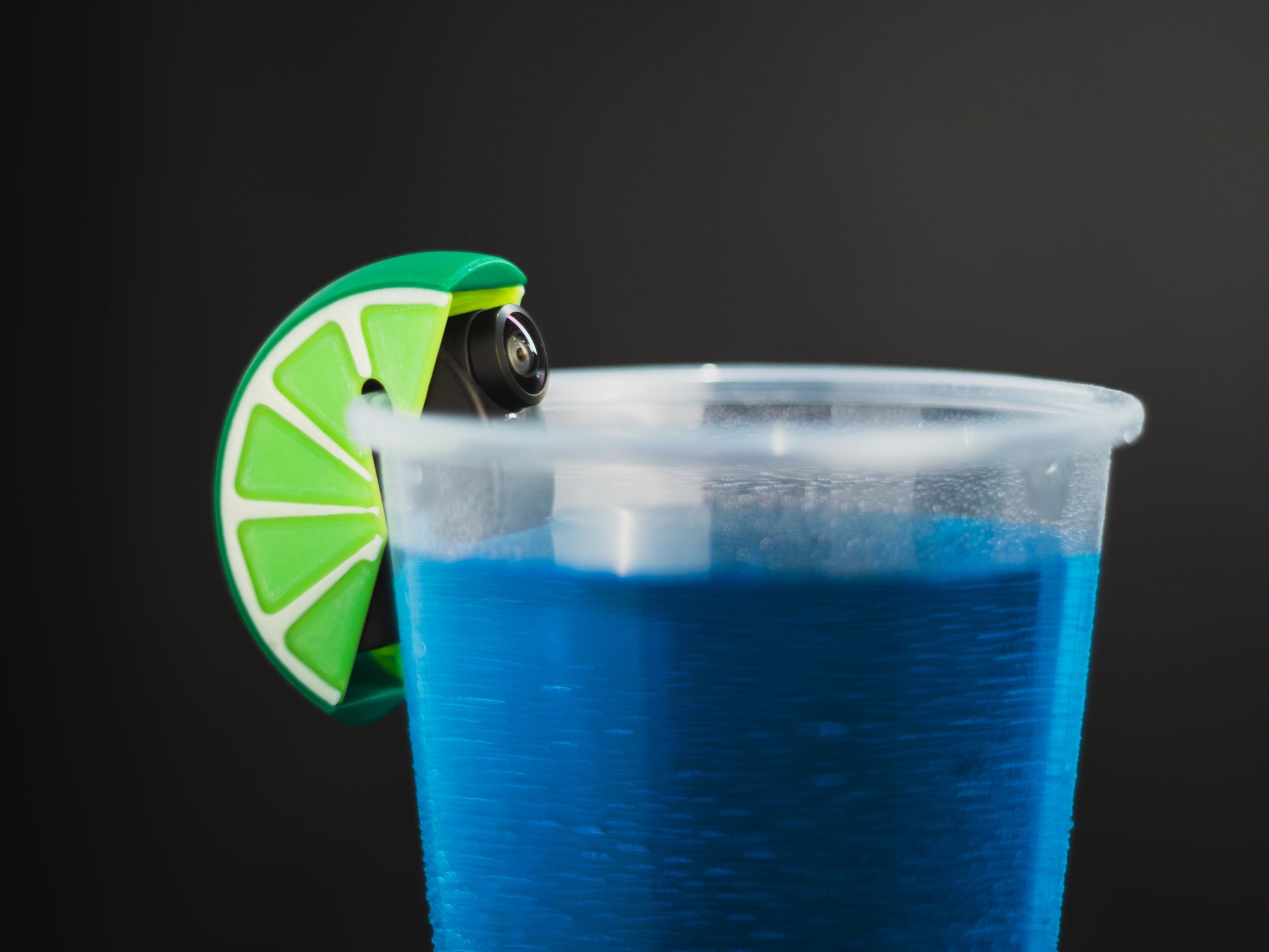 Blue drink in a plastic cup with a lime wheel garnish on a black background